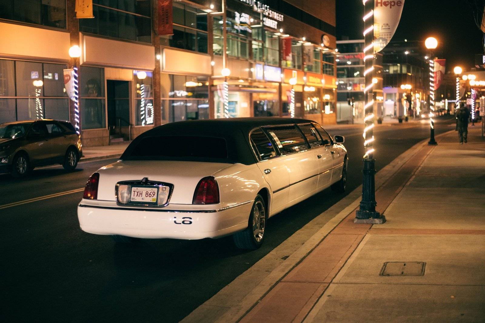 Blog White limo with tinted glasses and license plate on roadway against buildings illuminated by street lights in evening city